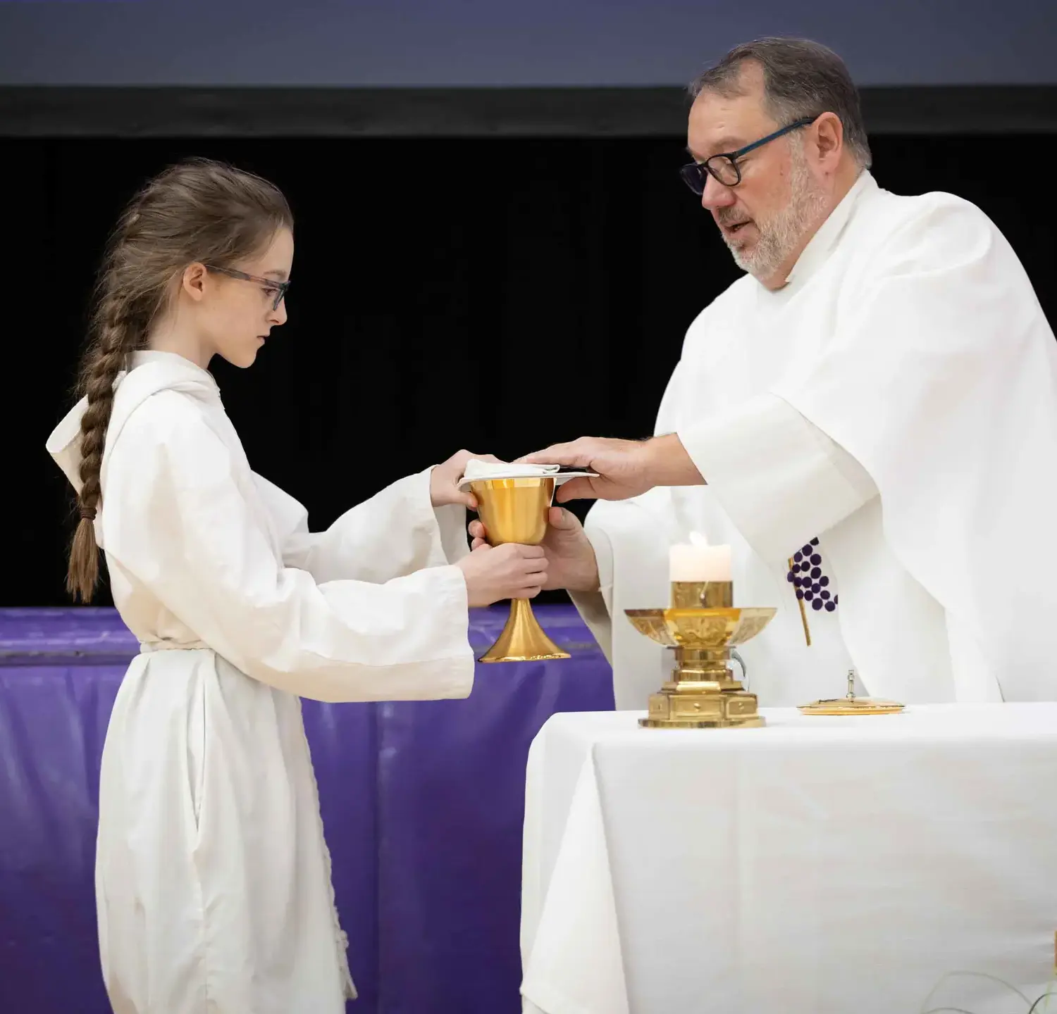 Notre Dame de Sion Grade School student and priest with communion wine at the alter.