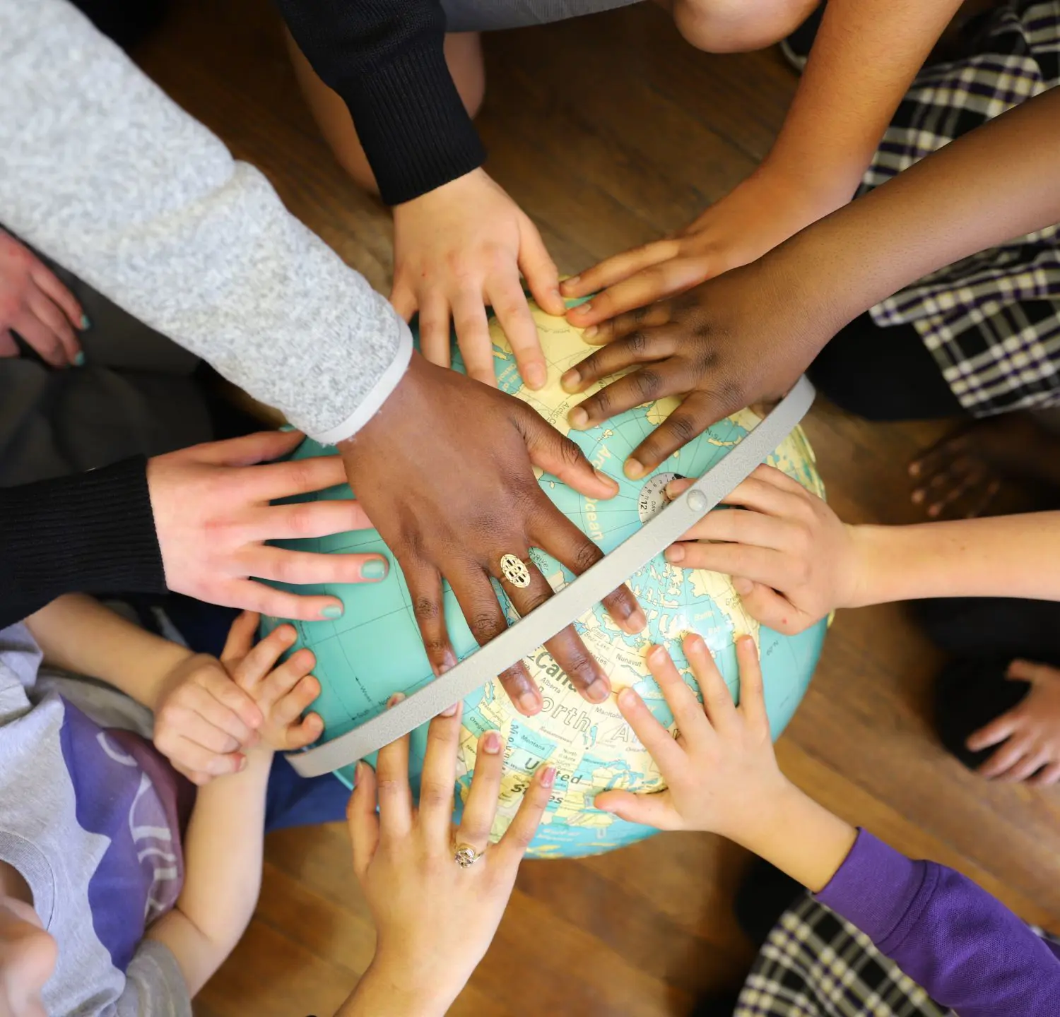 Notre Dame de Sion students and teacher resting their hands on the top of a globe.