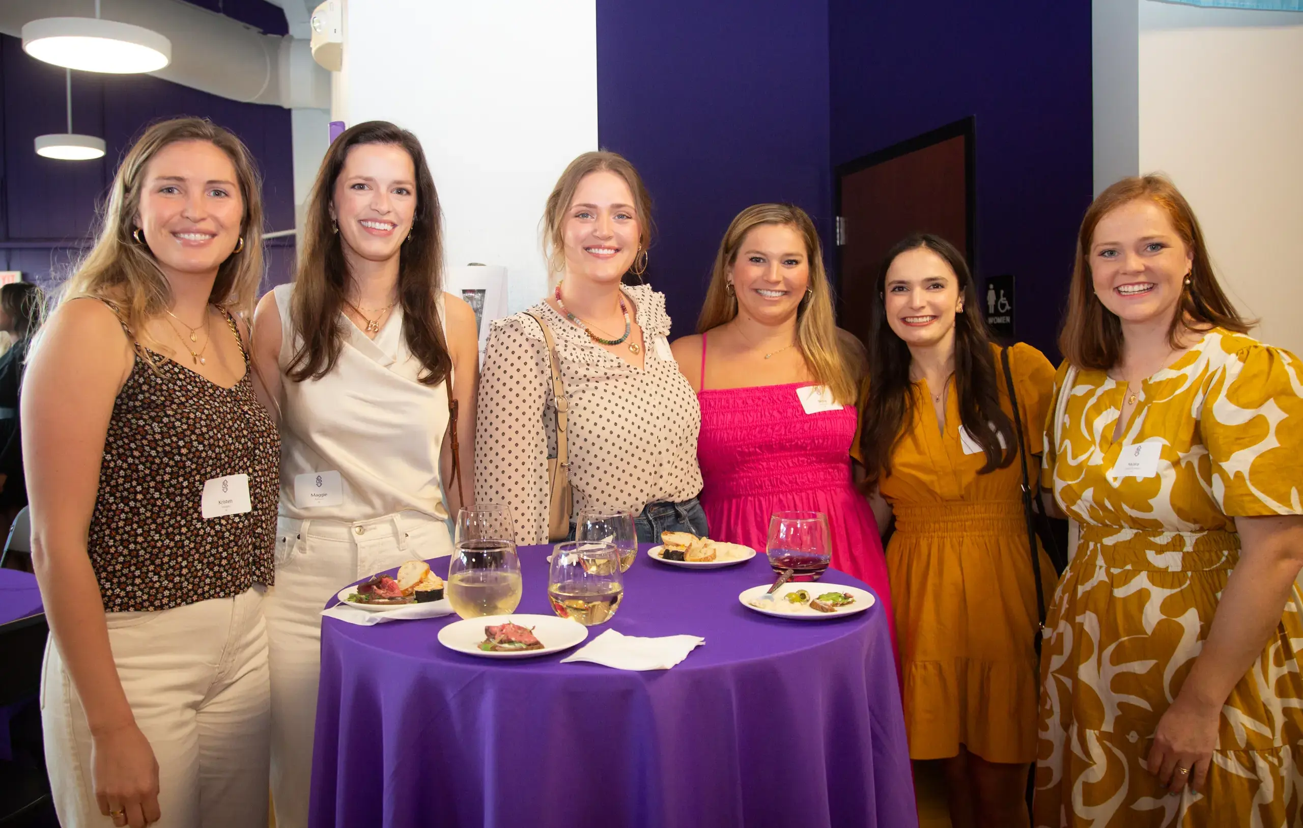 Notre Dame de Sion Alumna smiling for a group photograph at a high school reunion event, food and drinks on table in foreground.