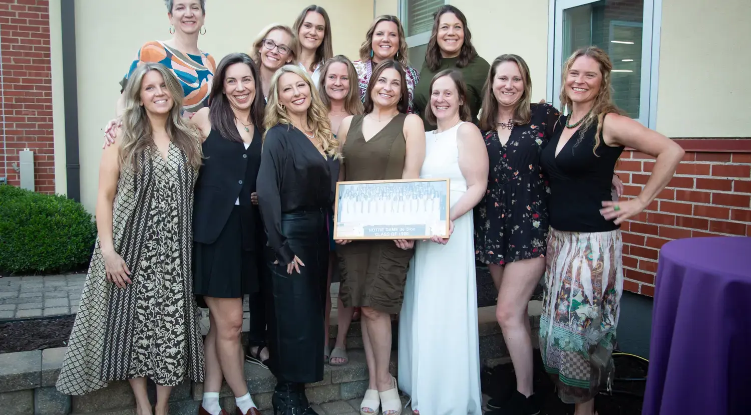 Group of Notre Dame de Sion alumna smiling happily, holding class photograph.