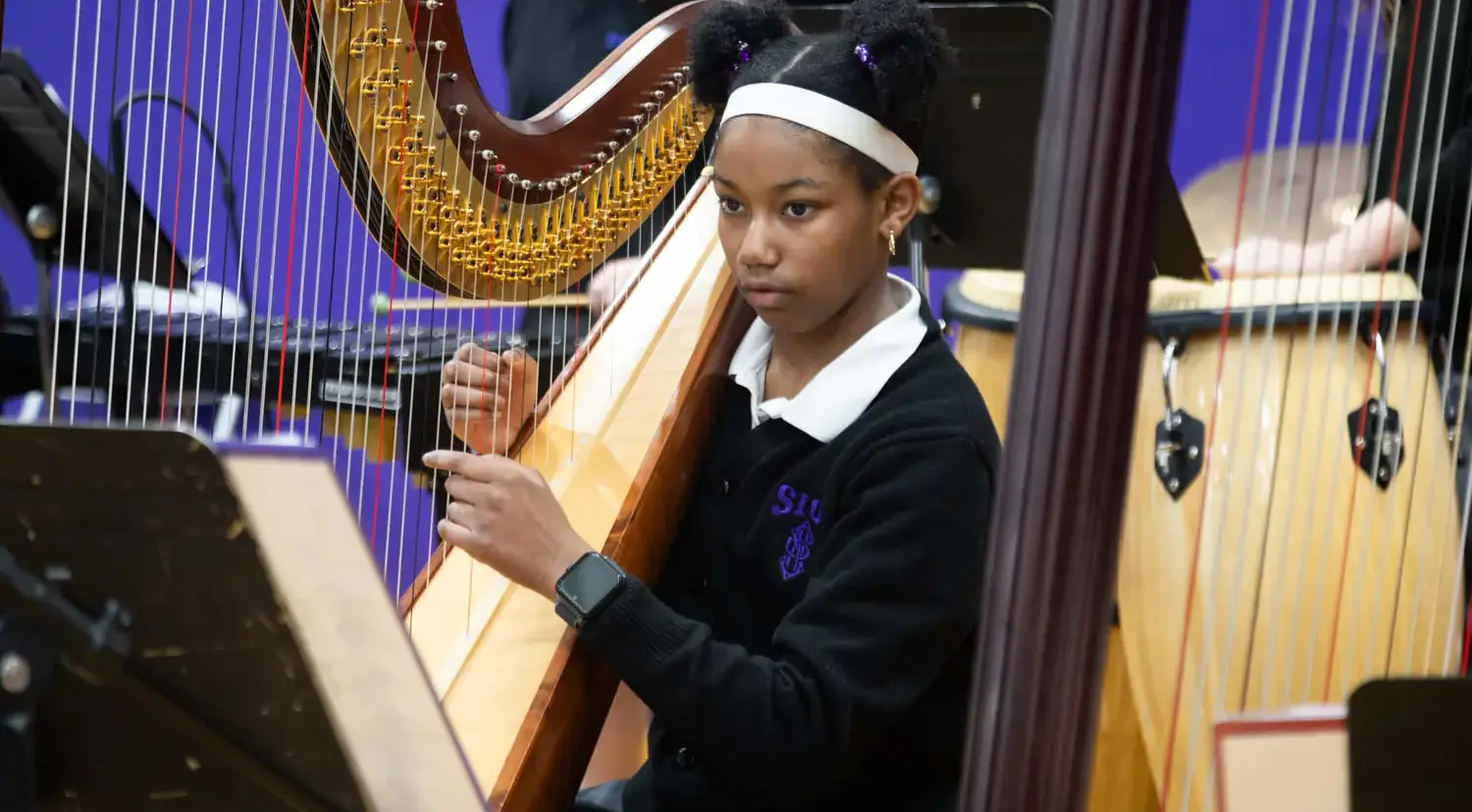 Notre Dame de Sion High School student playing the harp in an ensemble.