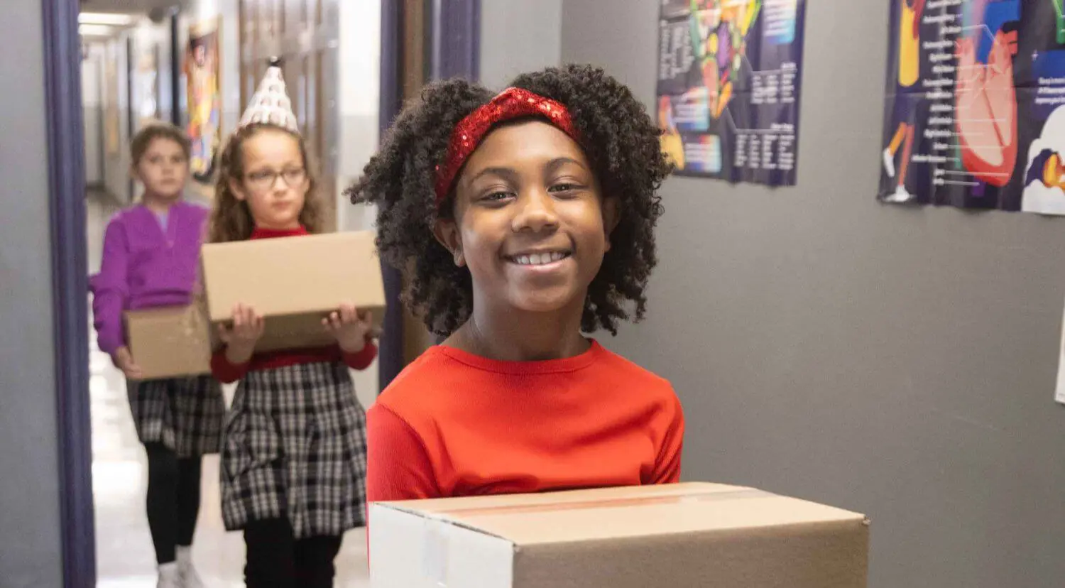 Notre Dame de Sion Grade School students carrying boxes and smiling as part of service and stewardship program.