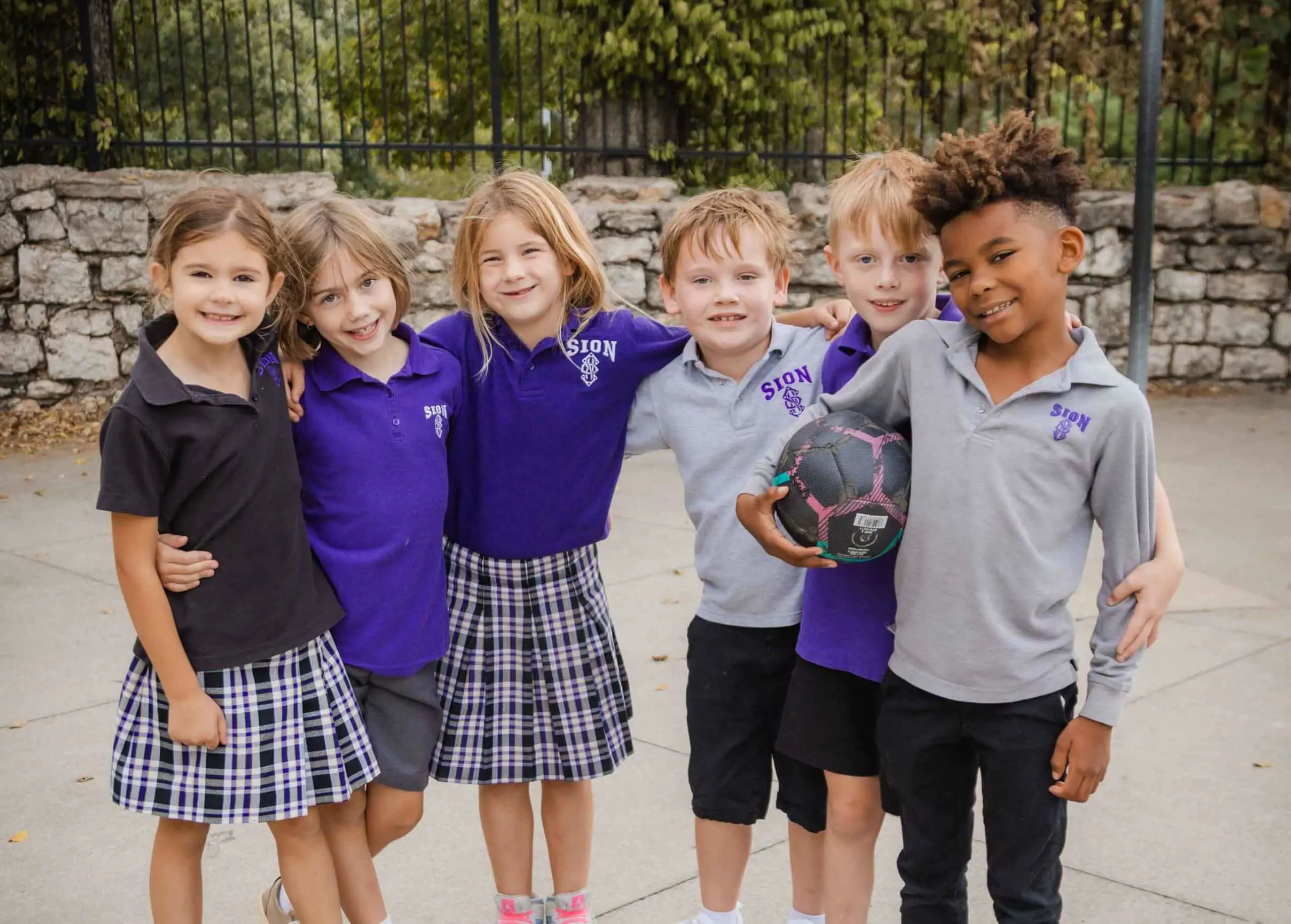 Notre Dame de Sion Grade School students smiling brightly, arm in arm in the playground at recess.