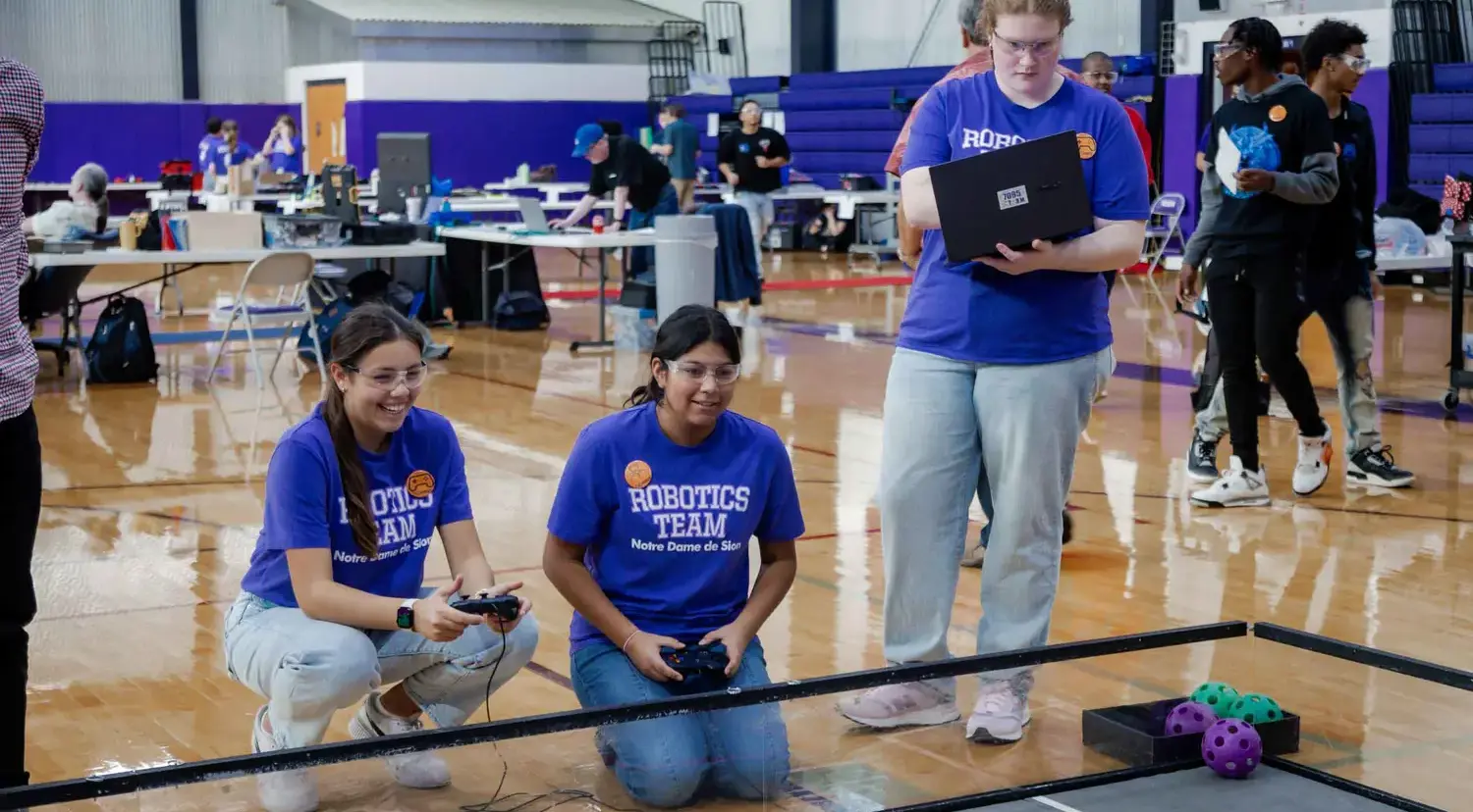 Notre Dame de Sion High School student robotics team driving robots with remote controls.