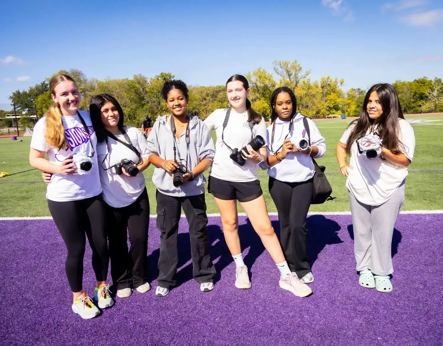 Notre Dame de Sion High School students with cameras, smiling elatedly, view of athletics field and running track.