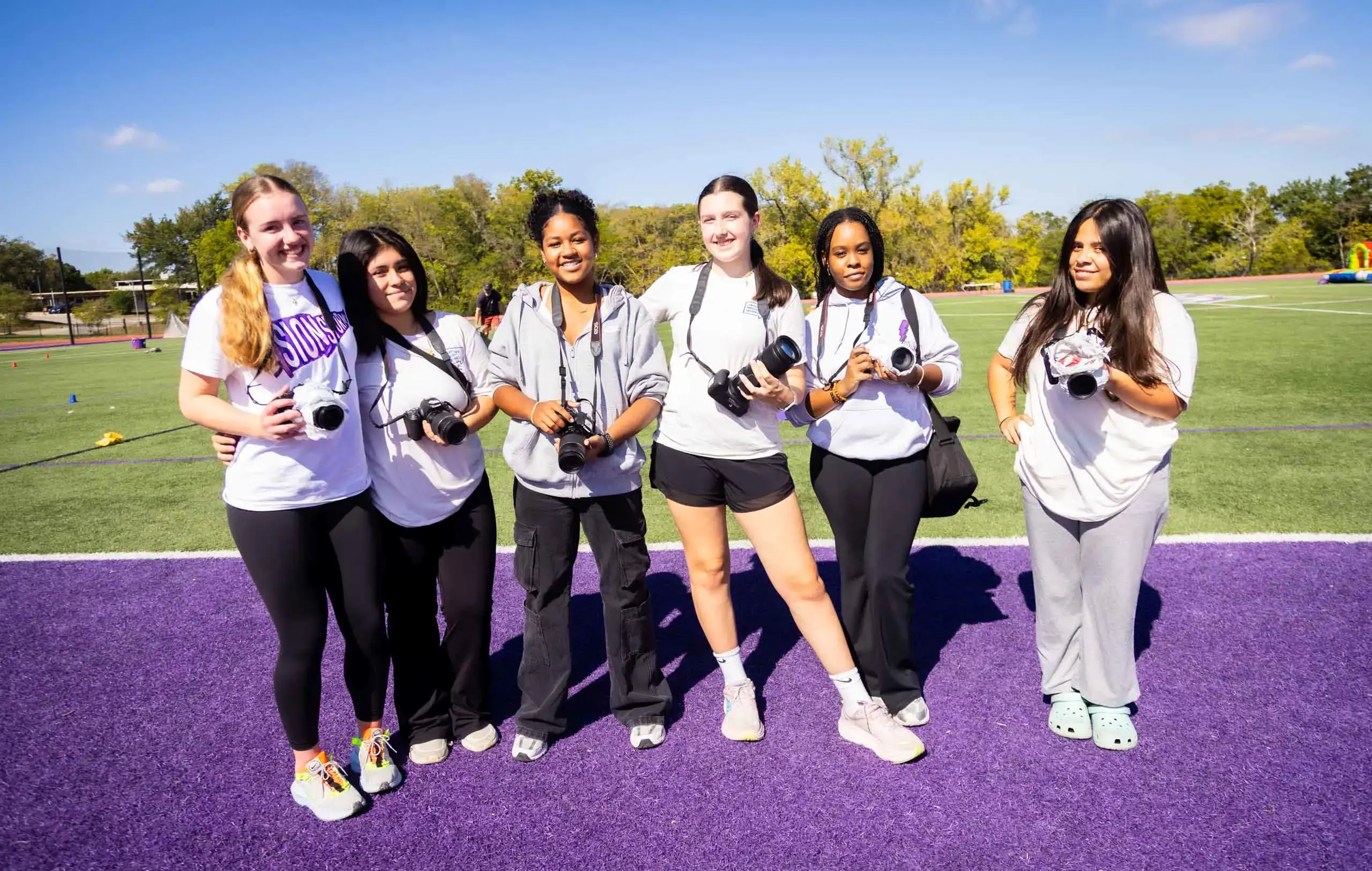 Notre Dame de Sion High School students with cameras, smiling elatedly, view of athletics field and running track.