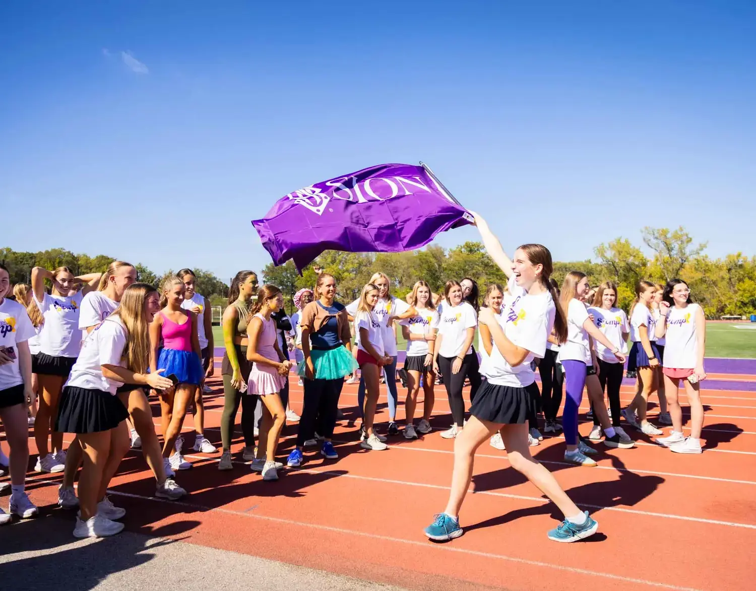 Notre Dame de Sion High School student waving Sion flag on sports track wearing sports kit, students crowding around.