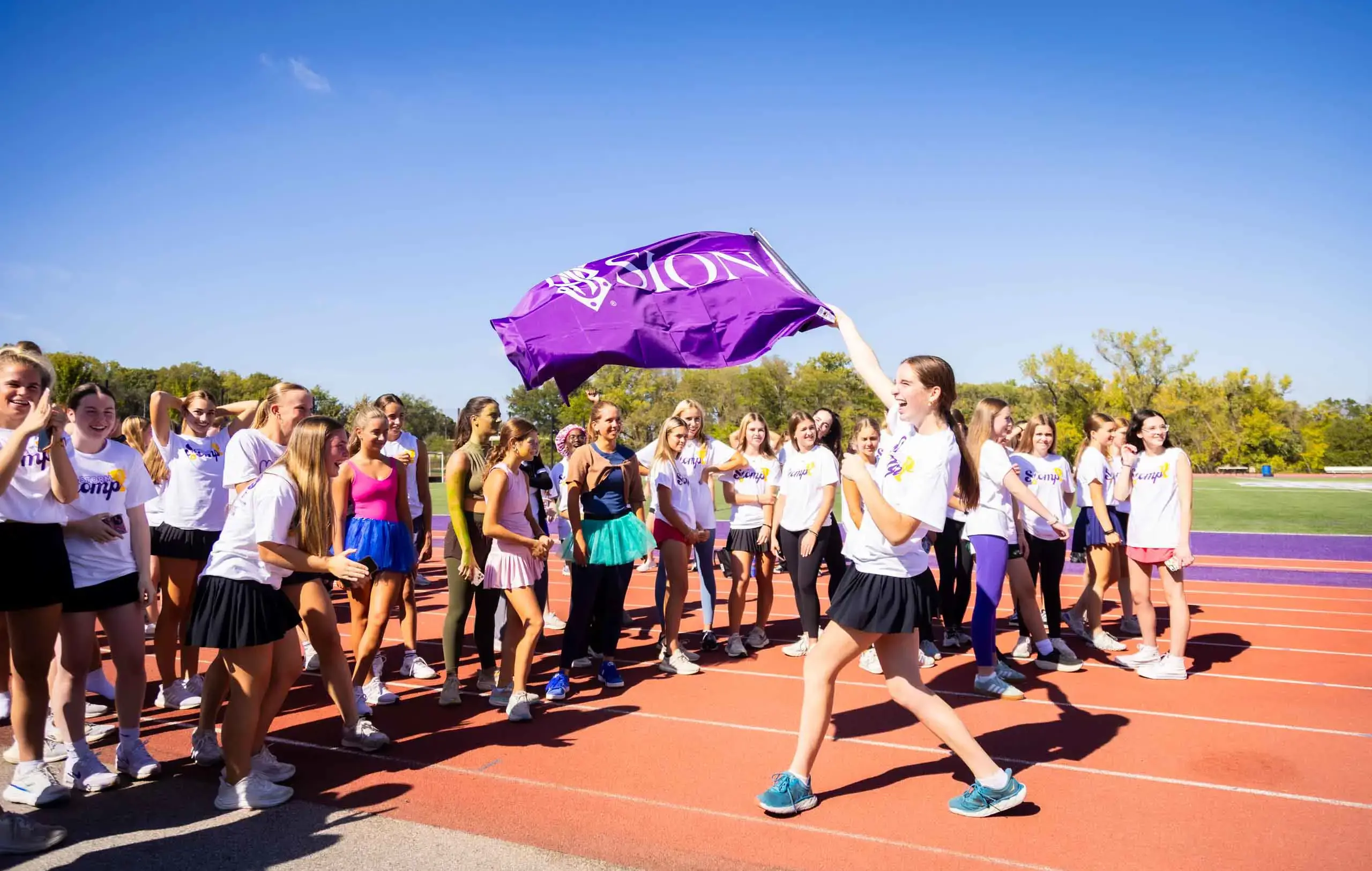 Notre Dame de Sion High School student waving Sion flag on sports track wearing sports kit, students crowding around.