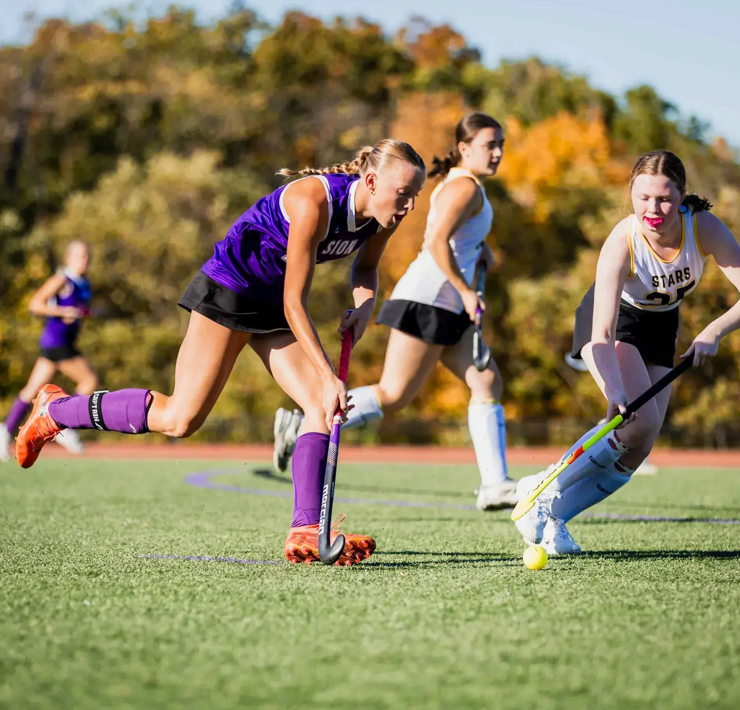 Notre Dame de Sion High School students playing field hockey on a sunny day.