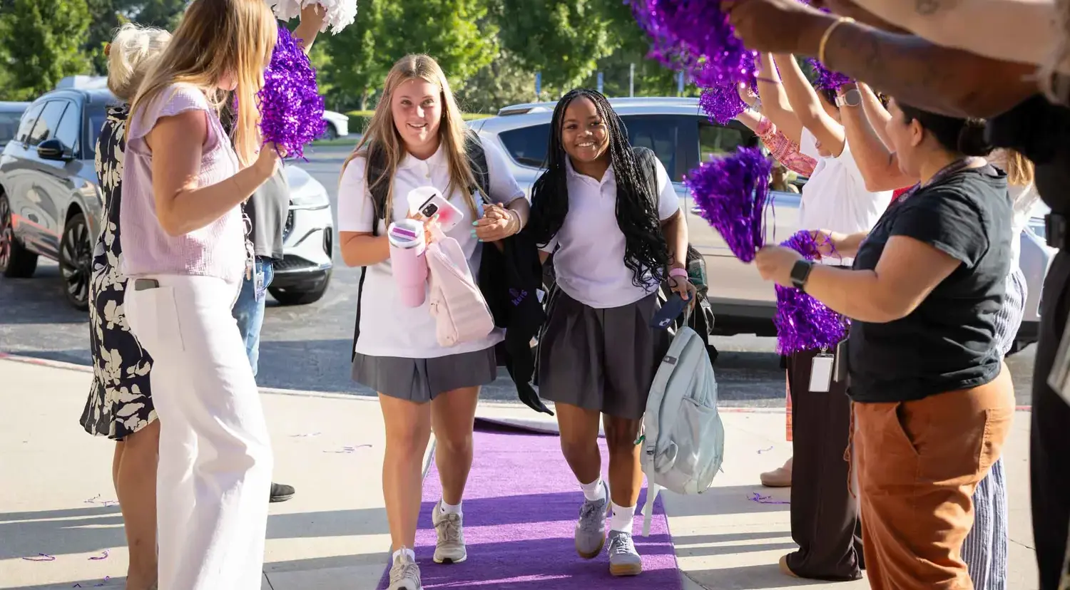 Notre Dame de Sion High School students entering school, walking on purple carpet, teachers cheering and waving purple pompoms.